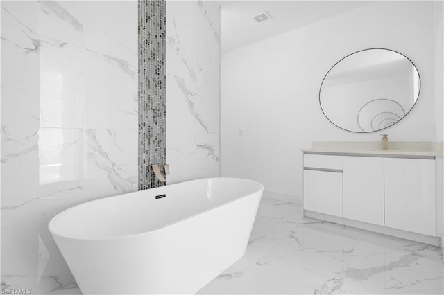 full bath with marble finish floor, visible vents, a freestanding bath, vanity, and stone wall