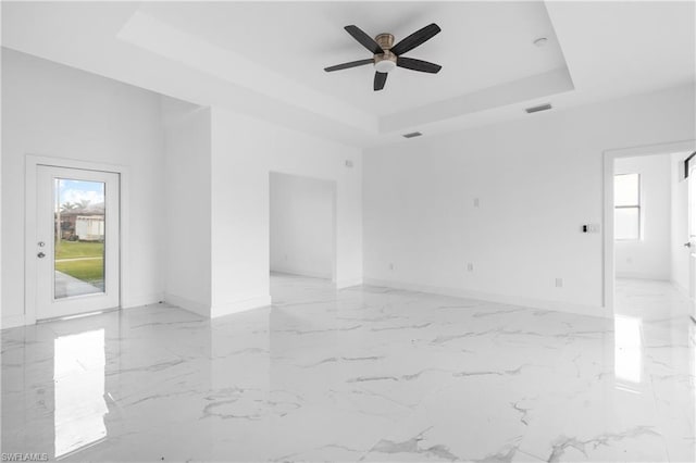 empty room featuring a raised ceiling, visible vents, marble finish floor, and baseboards