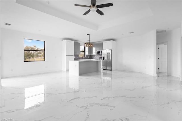 kitchen featuring a kitchen island, white cabinets, hanging light fixtures, appliances with stainless steel finishes, and a tray ceiling