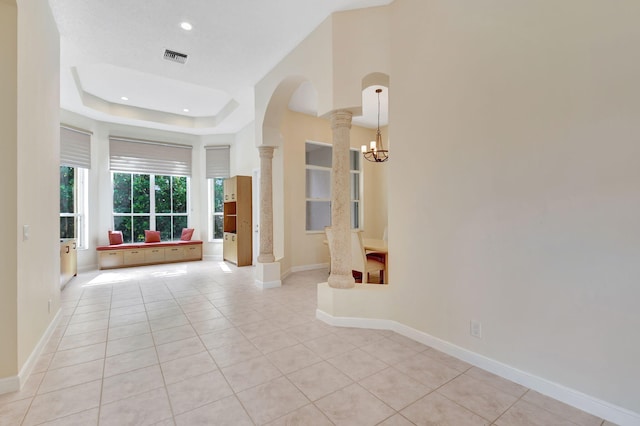 hall featuring a raised ceiling, light tile patterned flooring, a chandelier, and ornate columns