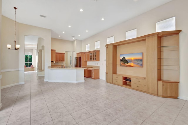 unfurnished living room featuring arched walkways, recessed lighting, a towering ceiling, a chandelier, and baseboards