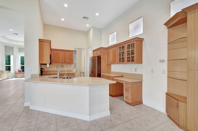 kitchen featuring light tile patterned flooring, stainless steel refrigerator, sink, a high ceiling, and kitchen peninsula