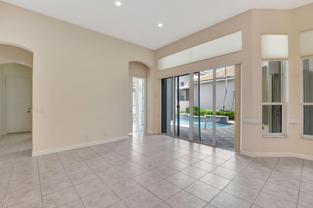 empty room featuring recessed lighting, arched walkways, baseboards, and light tile patterned floors