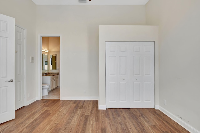 unfurnished bedroom featuring a closet, ensuite bathroom, baseboards, and wood finished floors