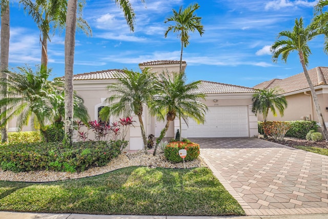 mediterranean / spanish-style house with decorative driveway, an attached garage, a tile roof, and stucco siding