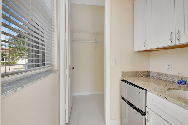 kitchen featuring white cabinetry, light tile patterned floors, light stone countertops, and sink