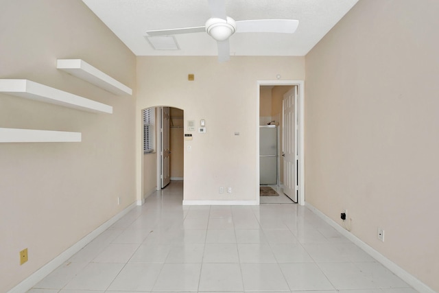 spare room featuring light tile patterned floors, baseboards, arched walkways, and a ceiling fan