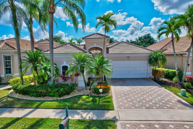 mediterranean / spanish house featuring a garage, a tiled roof, decorative driveway, and stucco siding