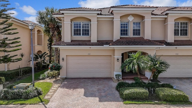 mediterranean / spanish house featuring a garage, decorative driveway, a tile roof, and stucco siding