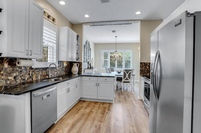 kitchen featuring tasteful backsplash, appliances with stainless steel finishes, a peninsula, white cabinetry, and a sink