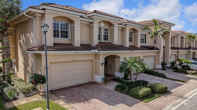 view of front facade featuring a garage, a tiled roof, decorative driveway, and stucco siding