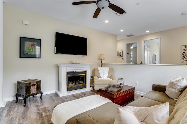 living room with a glass covered fireplace, wood finished floors, visible vents, and recessed lighting