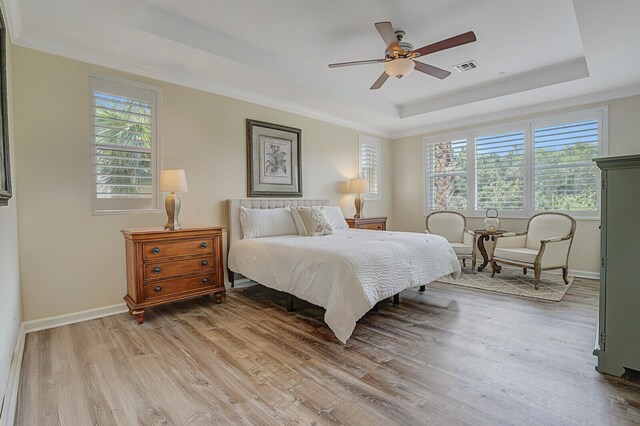 bedroom with light wood-type flooring, a raised ceiling, visible vents, and baseboards