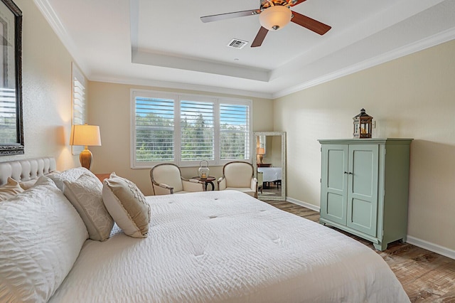 bedroom featuring baseboards, visible vents, a tray ceiling, and wood finished floors