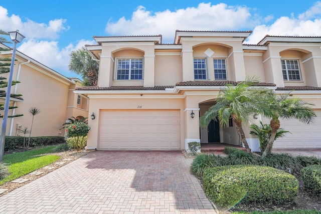 mediterranean / spanish-style home with decorative driveway, a tile roof, an attached garage, and stucco siding