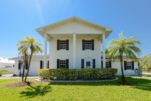 greek revival inspired property with brick siding and a front yard