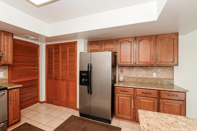 kitchen with stainless steel refrigerator with ice dispenser, light tile patterned floors, tasteful backsplash, light stone counters, and brown cabinetry