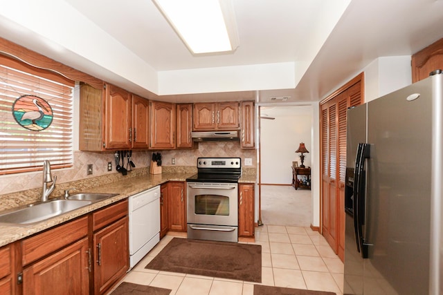 kitchen featuring appliances with stainless steel finishes, a sink, under cabinet range hood, brown cabinetry, and light tile patterned floors