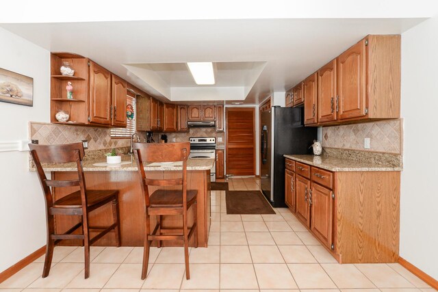 kitchen with appliances with stainless steel finishes, a peninsula, a raised ceiling, and decorative backsplash