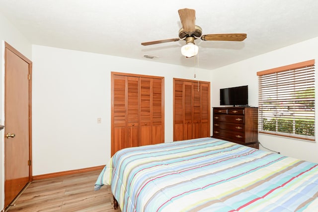 bedroom with light wood-style floors, two closets, a ceiling fan, and baseboards