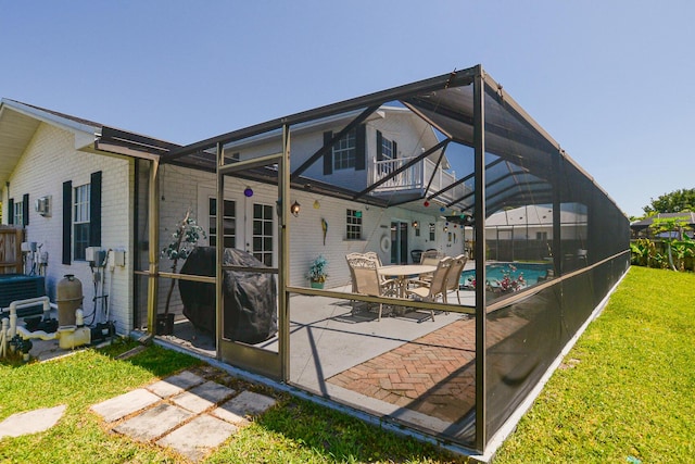 rear view of house featuring brick siding, a patio, a lawn, and glass enclosure