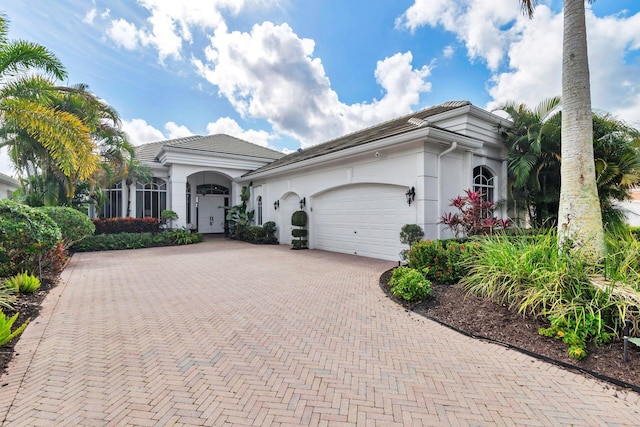 mediterranean / spanish-style house featuring decorative driveway, a tiled roof, an attached garage, and stucco siding