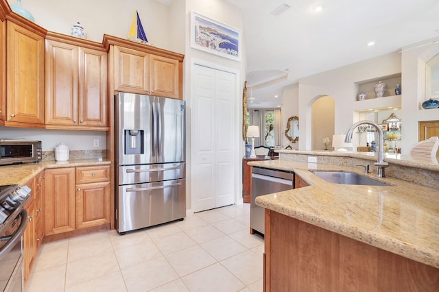 kitchen featuring light tile patterned floors, stainless steel appliances, light stone counters, and a sink