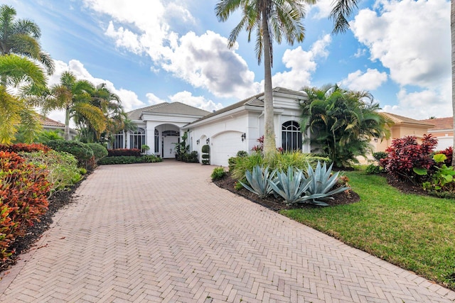 mediterranean / spanish home featuring a garage, a front lawn, decorative driveway, and stucco siding