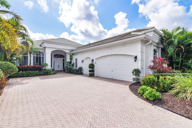 view of front of house with a garage, a tile roof, decorative driveway, and stucco siding