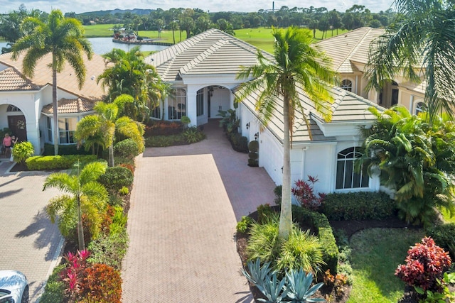 view of front facade featuring a water view, a tile roof, decorative driveway, and stucco siding