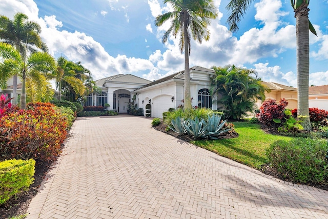 mediterranean / spanish-style home with a front yard, decorative driveway, an attached garage, and stucco siding