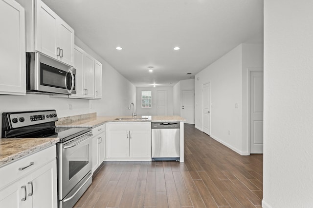 kitchen with stainless steel appliances, a peninsula, a sink, white cabinetry, and dark wood finished floors