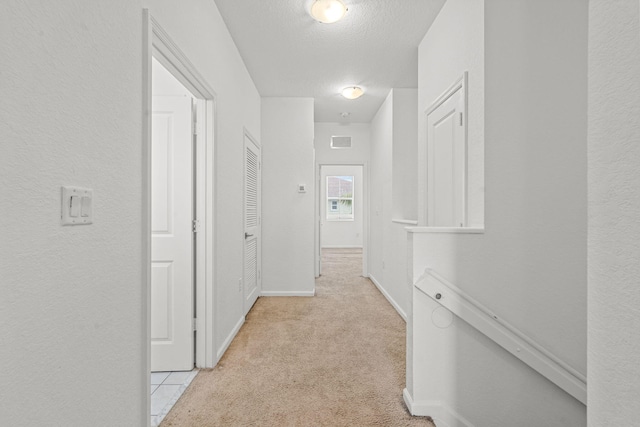 hallway with visible vents, light carpet, a textured ceiling, and baseboards