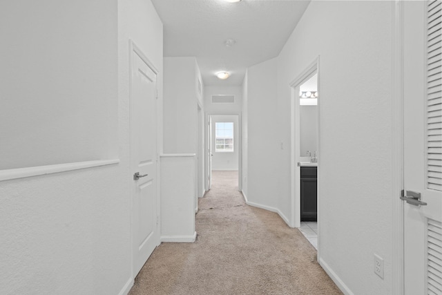 hallway featuring light carpet, visible vents, and baseboards