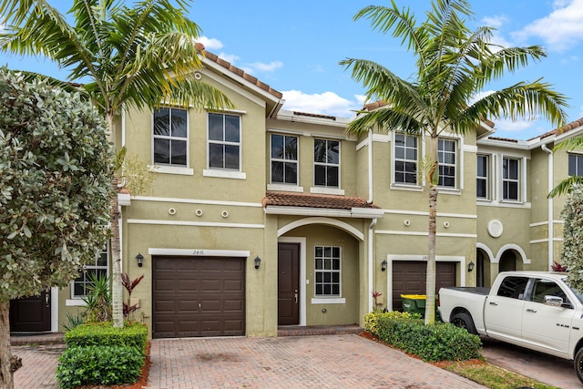 townhome / multi-family property featuring decorative driveway, a tile roof, an attached garage, and stucco siding