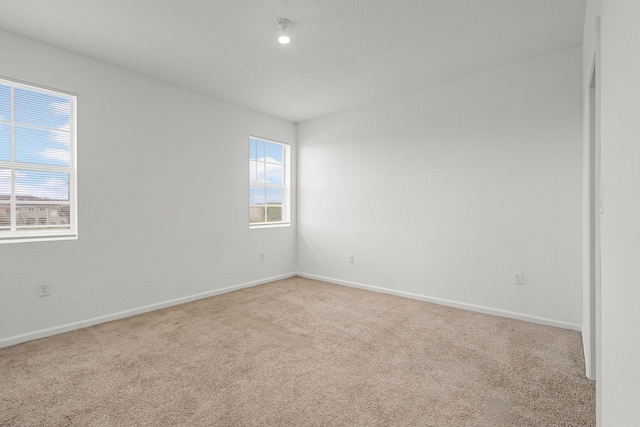 spare room with a healthy amount of sunlight, baseboards, and light colored carpet