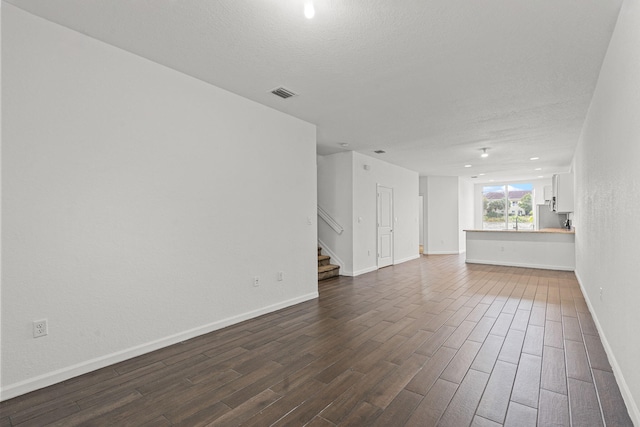 unfurnished room with dark wood-style floors, visible vents, stairway, a textured ceiling, and baseboards