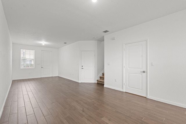 spare room featuring stairway, dark wood-style flooring, visible vents, and baseboards