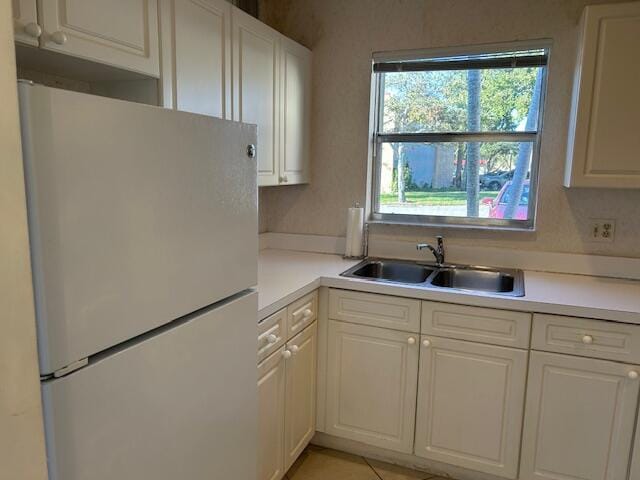 kitchen featuring white refrigerator, light tile patterned floors, sink, and white cabinets