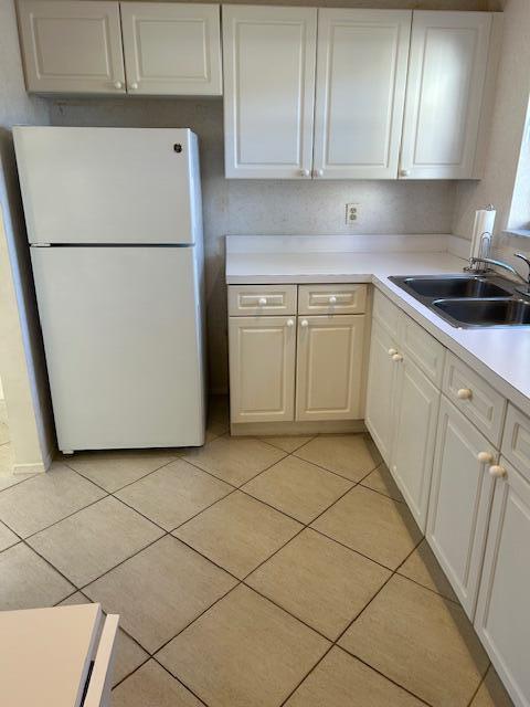 kitchen featuring white cabinetry, sink, light tile patterned flooring, and white fridge