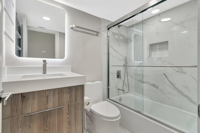 full bathroom with vanity, bath / shower combo with glass door, and toilet