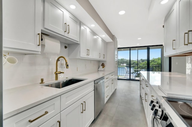 kitchen featuring sink, a water view, appliances with stainless steel finishes, a wall of windows, and white cabinets