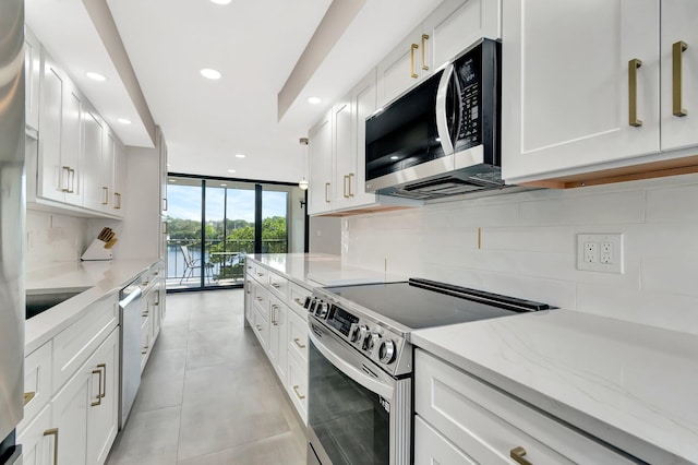 kitchen featuring appliances with stainless steel finishes, tasteful backsplash, light stone countertops, expansive windows, and white cabinets