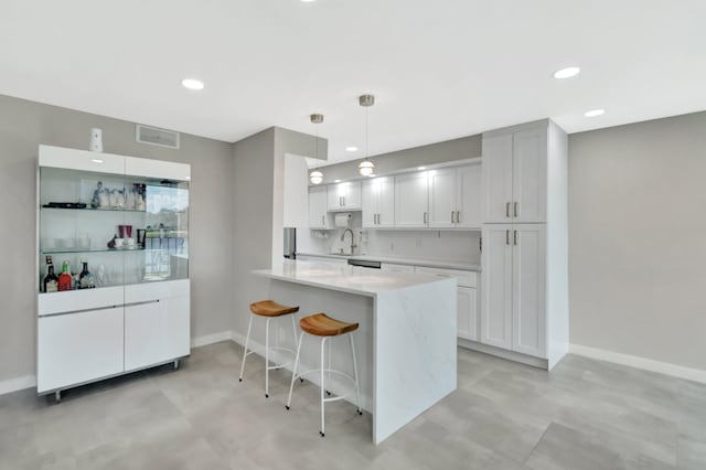 kitchen featuring a breakfast bar, decorative light fixtures, white cabinetry, sink, and kitchen peninsula