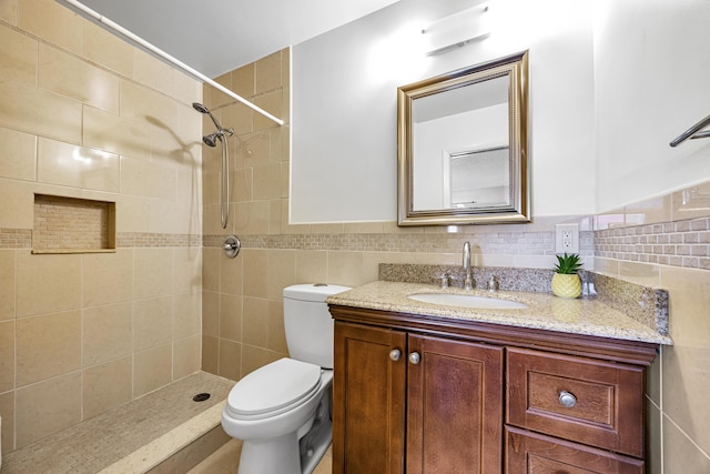 bathroom with vanity, tiled shower, tile walls, and toilet