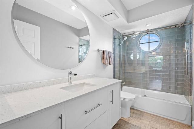 full bathroom featuring shower / bath combination with glass door, hardwood / wood-style floors, vanity, a textured ceiling, and toilet