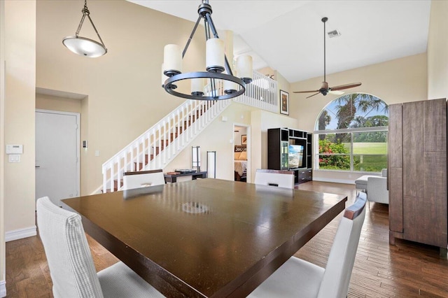 dining space with dark wood-type flooring, ceiling fan with notable chandelier, and high vaulted ceiling