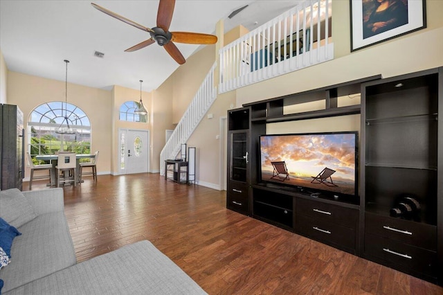 living room with dark wood-type flooring, ceiling fan, and a towering ceiling