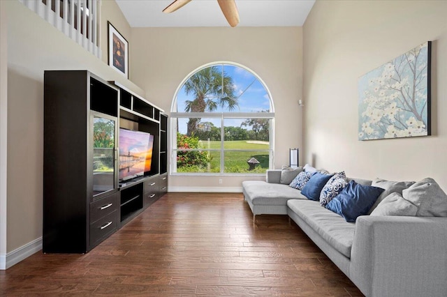 living room featuring dark wood-type flooring, ceiling fan, and a high ceiling