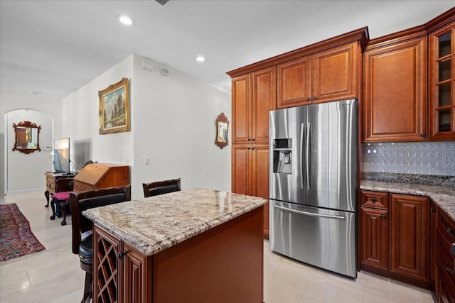 kitchen with light stone counters, backsplash, a kitchen island, and stainless steel refrigerator with ice dispenser